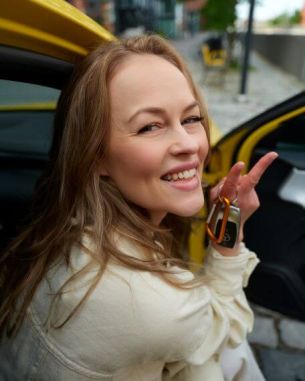 Kissanmaan Autokoulu Tampere – nuori nainen esittelee auton avaimia keltaisen auton vieressä